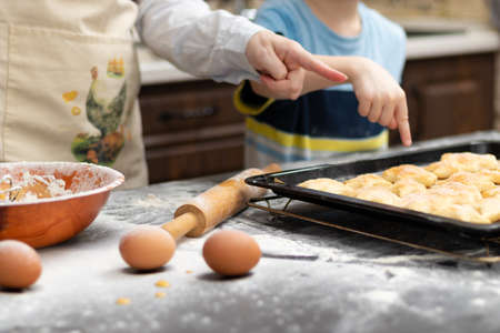 Mom and son try sweet puff pastry lying on parchment on a baking sheet at home in the kitchen. Nearby lies a rolling pin and a bowl. selective focus. portrait. close-upの写真素材