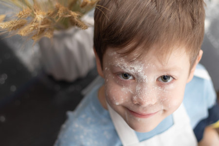 A cute boy prepares sweet cookies at home in the kitchen and plays with flour against the background...