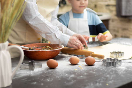 Mom and son are cutting out molds for baking sweet cookies from puff pastry on a black wooden table sprinkled with flour at home in the kitchen. selective focus. close-upの写真素材