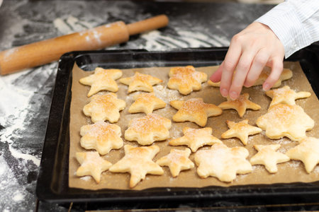 On a baking sheet with parchment, hot freshly baked puff sweet cookies against the background of a black kitchen table with spilled flour. selective focus. close-upの写真素材