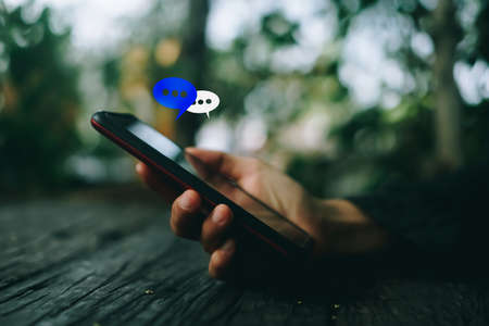 Women hand using smartphone typing, chatting conversation in chat box icons pop up. Social media maketing technology concept.Vintage soft color tone background.の写真素材