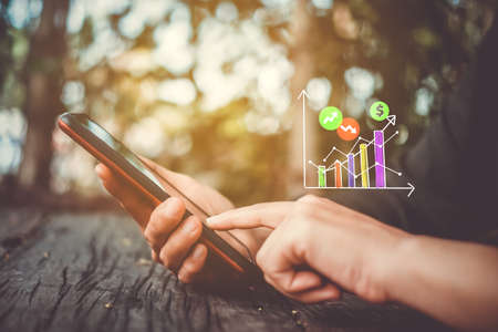 Woman hand using smartphone or tablet to do business, financial or trading stock forex market  with cafe bokeh vintage color tone background.の写真素材