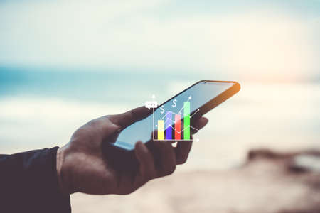 Woman hand using smartphone or tablet to do business, financial or trading stock forex market  with beach nature backgroundの写真素材