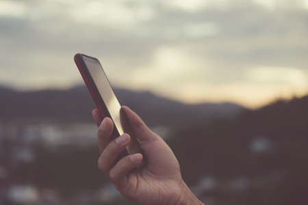 Woman hand using smartphone or tablet to do business, financial social network  with mountain view nature backgroundの写真素材