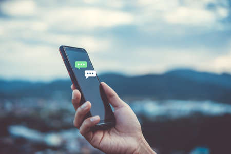 Women hand using smartphone typing, chatting conversation in chat box icons pop up. Social media maketing technology concept.Vintage soft color tone background.の写真素材
