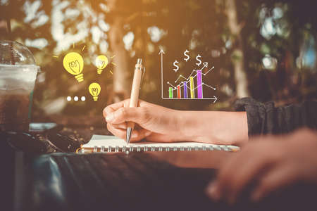 Copy space of woman hand writing down in white notebook with idea and graph icon  background.の写真素材