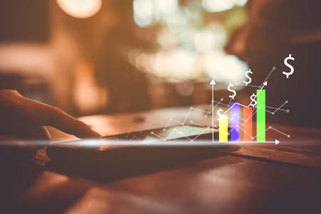 Woman hand using smartphone or tablet to do business, financial or trading stock forex market  with cafe bokeh vintage color tone background.の写真素材