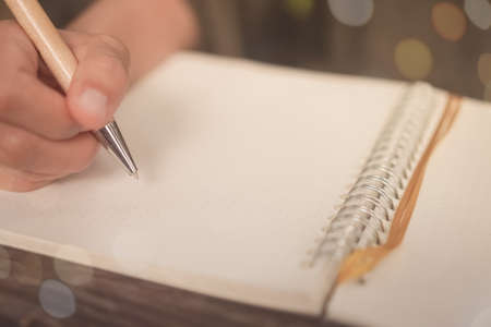 Copy space of woman's hand writing down in white notebook with sun light background.の写真素材