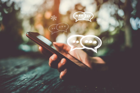 Woman's hand using smartphone typing, chatting conversation in chat box icons pop up. Social media...