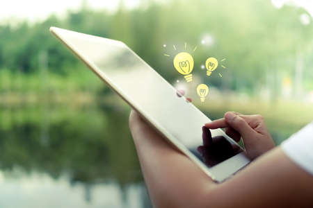 Woman's hands using big tablet to do work, planning, reading and idea icon pop up in nature park.の写真素材