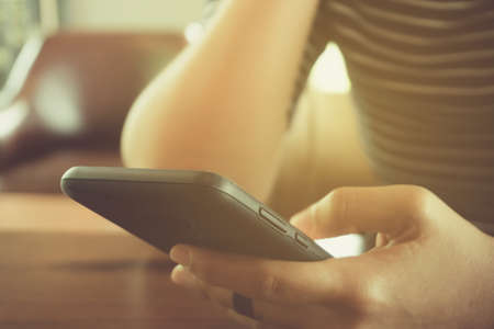 Woman hand using smartphone and laptop with cafe shop colorful highlight shade to object beautiful background. Business, financial, trade stock maket and social network concept.の写真素材