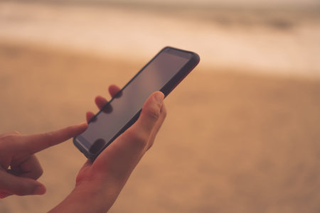Woman hand using smartphone beautiful nature tropical beach ocean background. Business, financial,...