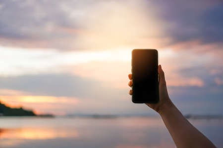 Woman hand using smartphone beautiful nature tropical beach ocean background. Business, financial, trade stock maket and social network concept.の写真素材