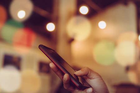 Woman hand using smartphone and laptop with cafe shop colorful beautiful bokeh background. Business, financial, trade stock maket and social network concept.の写真素材