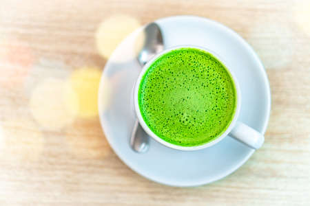 A white cup of green tea latte on wood table in coffee cafe with bokeh warm and relax color tone style.の写真素材