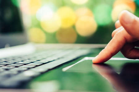 Woman hand finger press on laptop to work or study with cafe shop colorful beautiful bokeh background. Business, financial, trade stock maket and social network concept.の写真素材