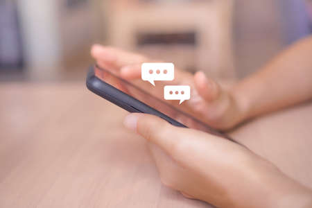 Women hand using smartphone typing, chatting conversation in chat box icons pop up. Social media maketing technology concept.Vintage soft color tone background.の写真素材