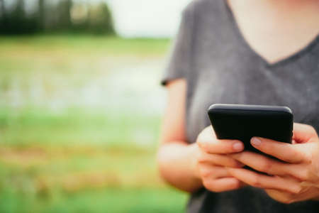 Woman hand using smartphone with nature green  beautiful background. Business, financial, trade stock maket and social network concept.の写真素材