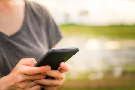 Woman hand using smartphone with nature green  beautiful background. Business, financial, trade stock maket and social network concept.の写真素材