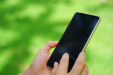 Woman hand using smartphone with nature green  beautiful background. Business, financial, trade stock maket and social network concept.の写真素材