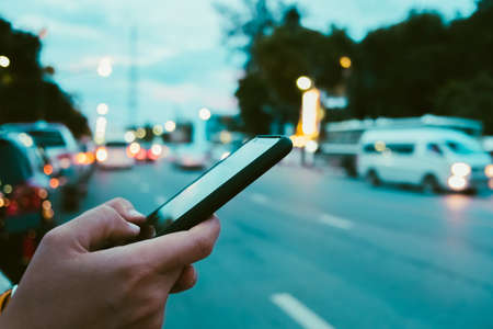 Woman hand using smartphone blur bokeh light road and vehicles background. Business, financial, trade stock maket and social network concept.の写真素材