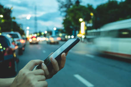 Woman hand using smartphone blur bokeh light road and vehicles background. Business, financial, trade stock maket and social network concept.の写真素材