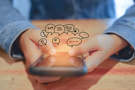 Women hand using smartphone typing, chatting conversation in chat box icons pop up. Social media maketing technology concept.Vintage soft color tone background.の写真素材
