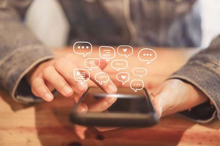 Women hand using smartphone typing, chatting conversation in chat box icons pop up. Social media maketing technology concept.Vintage soft color tone background.の写真素材