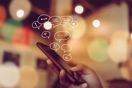 Women hand using smartphone typing, chatting conversation in chat box icons pop up. Social media maketing technology concept.Vintage soft color tone background.の写真素材