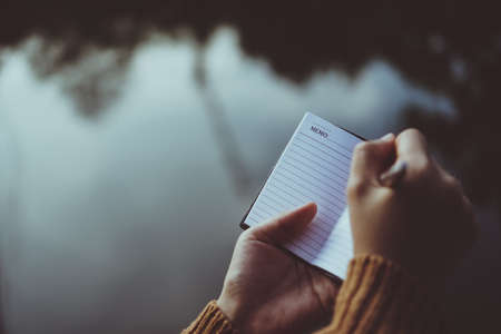 Woman hand writing down in small white memo notebook for take a note not to forget or to do list plan for future.の写真素材