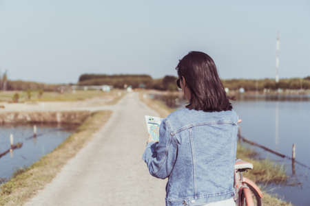 Woman ride bicycle in small road to nature while look at travel map background.の写真素材