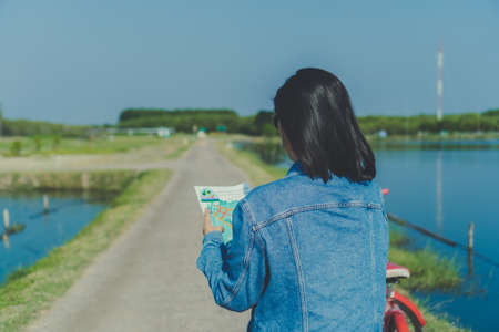 Woman ride bicycle in small road to nature while look at travel map background.の写真素材