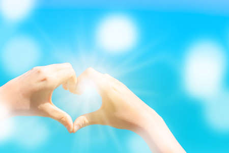 Woman hand do heart shape on blue sky  and bokeh background.の写真素材