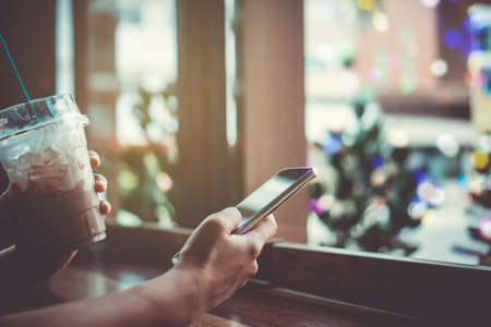 Woman hand using smartphone with cafe shop colorful beautiful bokeh background. Business, financial, trade stock maket and social network concept.の写真素材