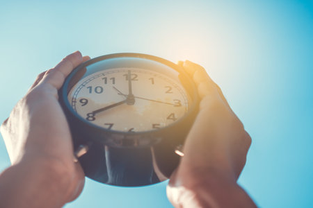 Selective focus of hands holding of alarm clock with nature bokeh background.