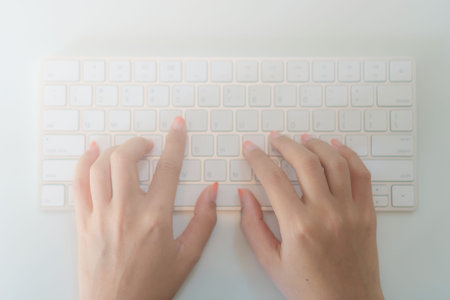 Top view of woman hand typing on white modern keyboard on table background.