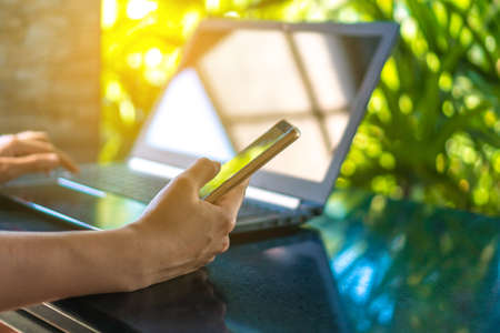 Woman hand using laptop and smartphone to work study with cafe shop colorful beautiful bokh background. Business, financial, trade stock maket and social network concept.の写真素材
