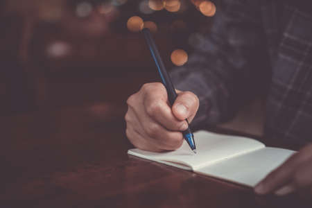 Woman hand writing down in small white memo notebook for take a note not to forget or to do list plan for future.の写真素材
