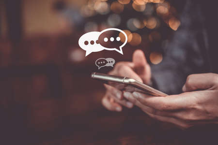 Women hand using smartphone typing, chatting conversation in chat box icons pop up. Social media marketing technology concept. Vintage soft color tone background.の写真素材