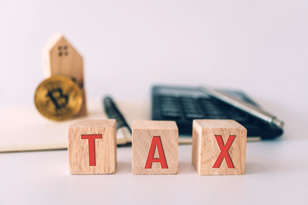 Tax word on wooden cube with objects as gold coin, calculator and mini home model behide white clean...