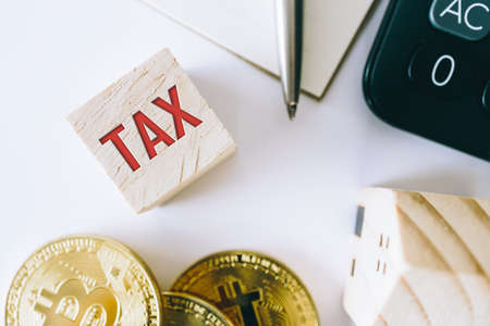 Tax word on wooden cube with objects as gold coin, calculator and mini home model behide white clean background. Business financial loan property concept.の写真素材