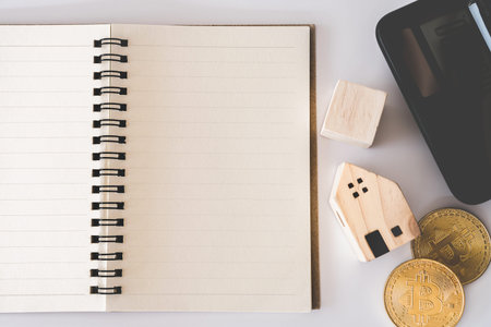Top view of blank white notebook with calculator, tiny home model, credit card and pen as frame...