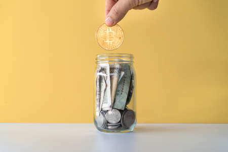 Hand drop gold Bitcoin the jar full of coin and bank notes meaning of saving investment with cryptocurrency digital money fintech online network. Business technology concept.の写真素材