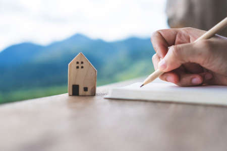 Woman hand writing down in small white memo notebook with jar full of money for plan wealth investing to do for future.の写真素材