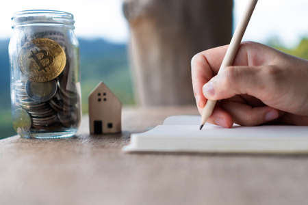 Woman hand writing down in small white memo notebook with jar full of money for plan wealth investing to do for future.の写真素材