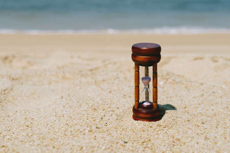 Small hourglass show time is flowing on sand beach texture background.の写真素材