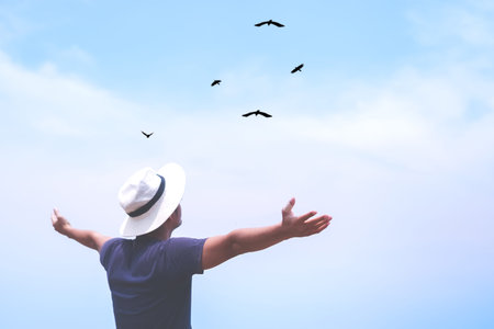 Man rise hands up to sky looking at birds fly through metaphor freedom concept with sunset sky and...