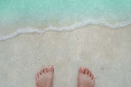 Top view of sand and water and woman foot onclean beach and white sand in summer with sun light blue sky and bokeh abstract  background.の写真素材