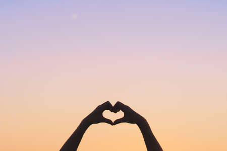 Woman hand do heart shape on sunset sky and bokeh background.の写真素材