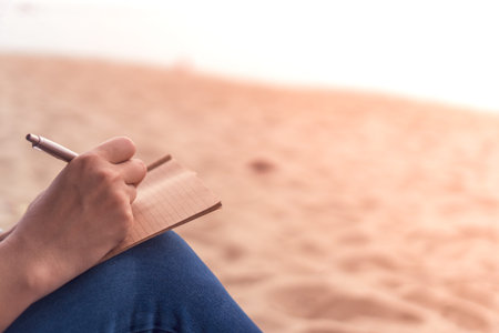 Woman hand writing down in small white memo notebook for take a note not to forget or to do list plan for future.の写真素材